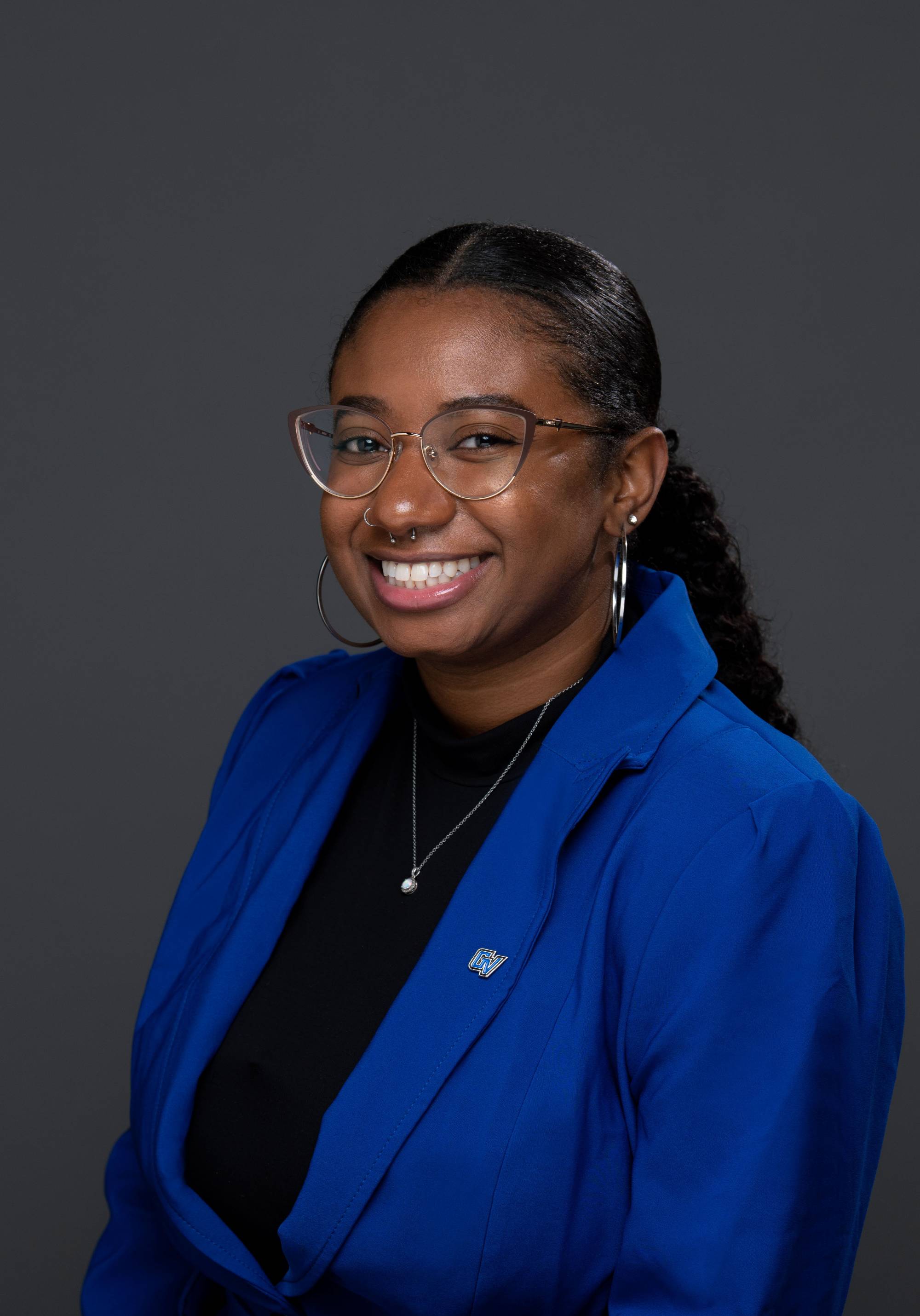 Young black woman with glasses and a blue blazer smiling at the camera